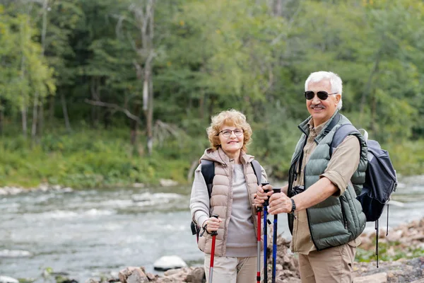 在夏天的日子里 那些背着背包和手杖在森林河边散步的活跃的老年夫妇们享受着他们的旅行 — 图库照片