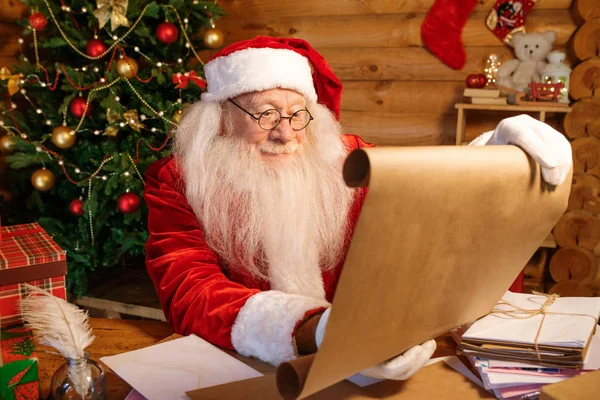 Santa Costume Unrolling Big Paper Christmas Wishes While Sitting Wooden — Stock Photo, Image
