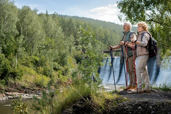 两个穿着活动服装 快乐而成熟的背包客站在林河边 一边旅行一边欣赏美丽的大自然 — 图库照片