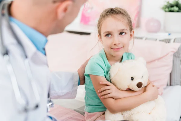 Cute Little Girl Puszystą Zabawką Patrząc Jej Lekarza Uśmiechem Słuchając — Zdjęcie stockowe
