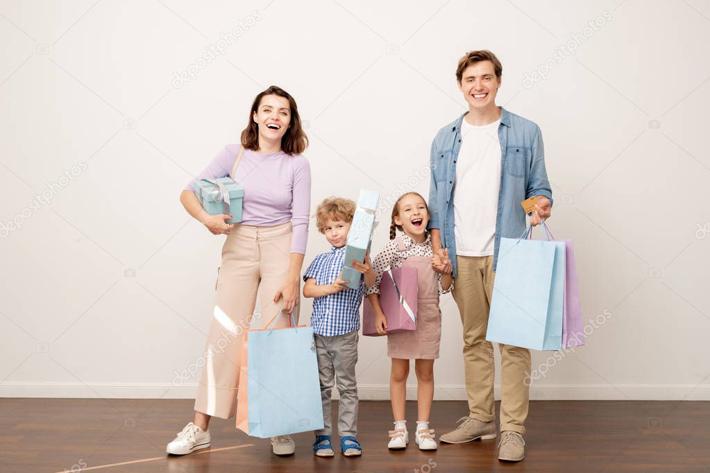 Laughing young parents with paperbags and giftboxes and their cheerful son and daughter feeling happy with shopping