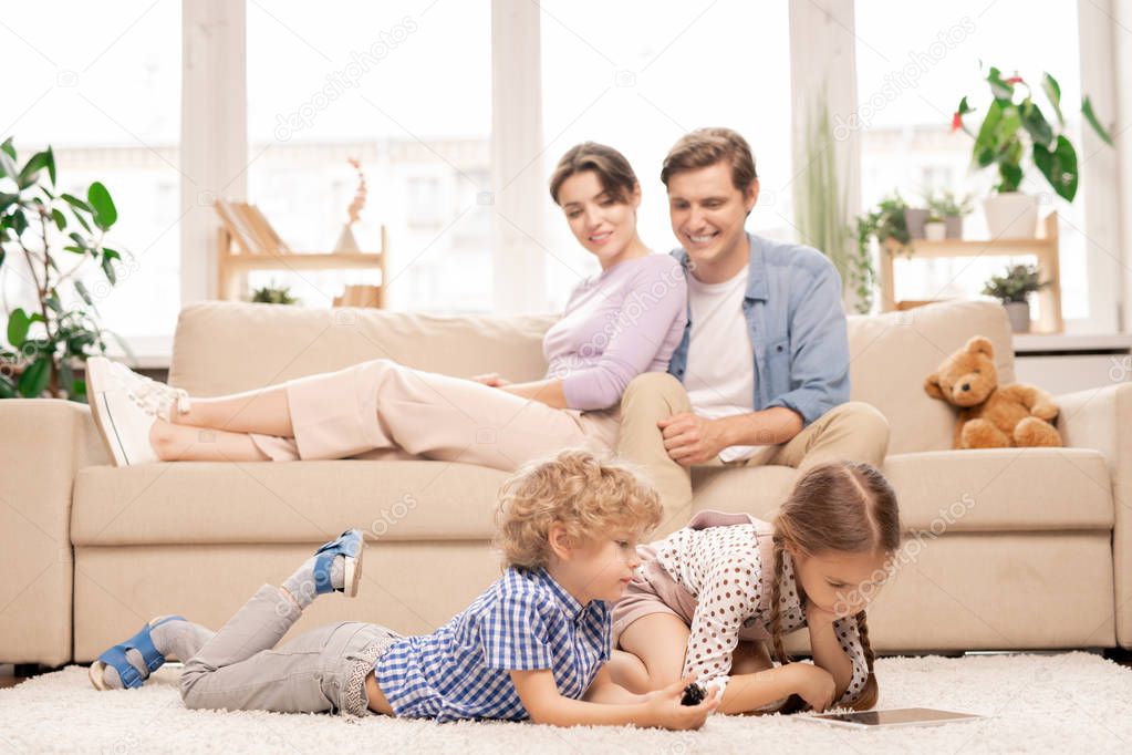 Two cute elementary age kids with touchpad lying on the floor of living-room while watching cartoons at home