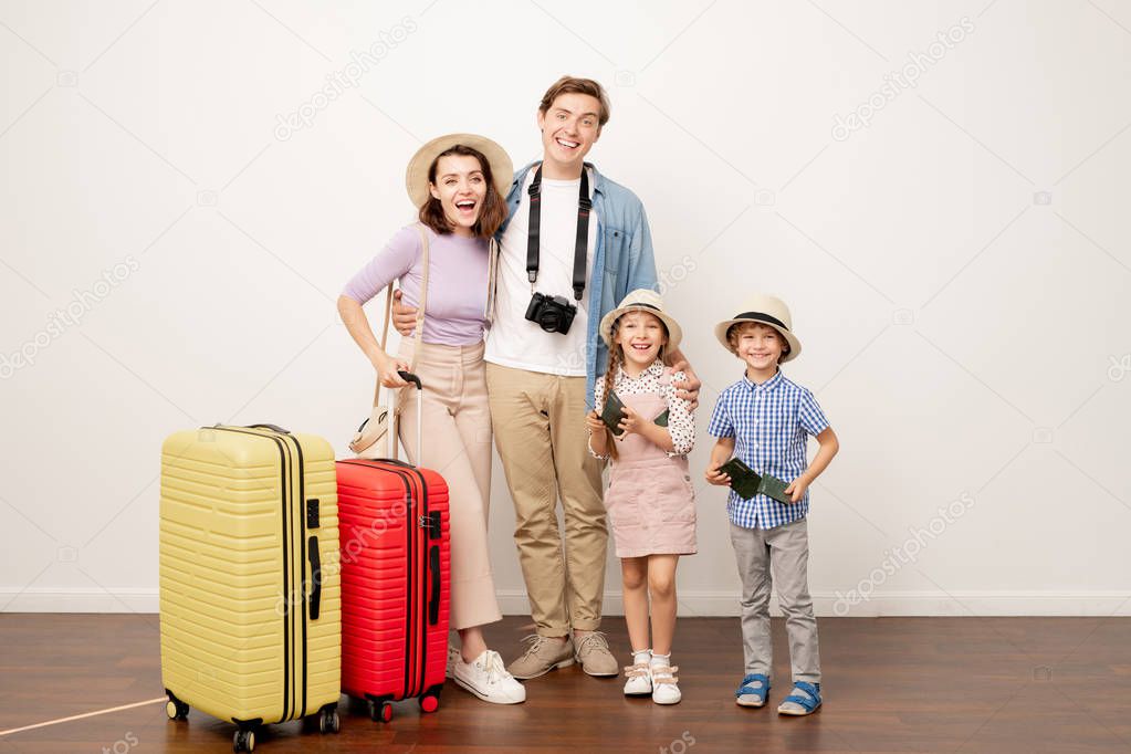 Young excited family of two parents and their cute kids in casualwear with suitcases ready for travel