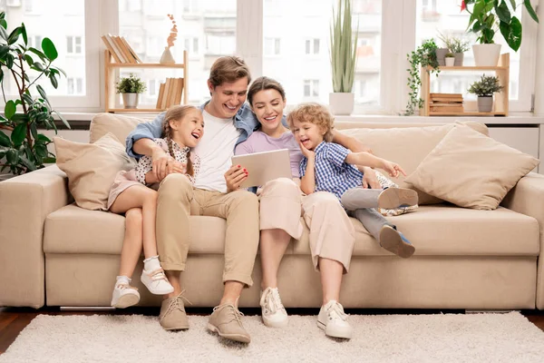 由两个孩子和一对夫妇组成的快乐的小家庭坐在沙发上 在触摸板上看滑稽的视频或卡通片 — 图库照片