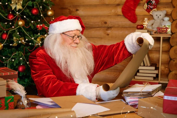快乐的圣诞老人 留着白胡子 坐在桌旁翻阅着写着圣诞祝福的信件 — 图库照片