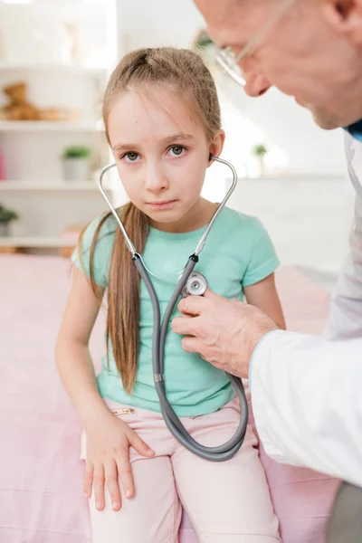 Menina Perplexa Ouvindo Seu Batimento Cardíaco Enquanto Médico Segurando Estetoscópio — Fotografia de Stock