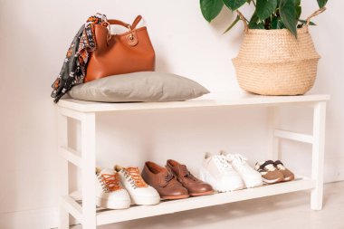 Koridorun bir kısmı beyaz raflı, yastıklı, deri çantalı, yeşil yerli bitkilerle dolu ve dört çift ayakkabılı bir daire.