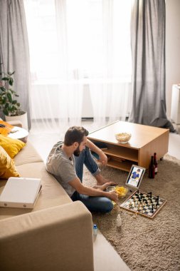 Genç sakallı adam arkadaşlarıyla satranç oynamaya odaklanmış. Ev izolasyonundaki tablette telekomünikasyon uygulaması kullanıyor.