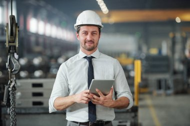 Endüstriyel sanayi atölyesinde tablet kullanan kasklı yakışıklı teknik mühendisin portresi