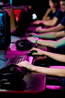 Çağdaş e-spor kulüpçülerinin bilgisayar monitörlerinin önünde masaların başında oturup siber oyunlar oynadığı bir sıra el.