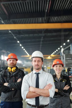 Confident factory team of professionals in hardhats standing with crossed arms in contemporary shop of large plant clipart