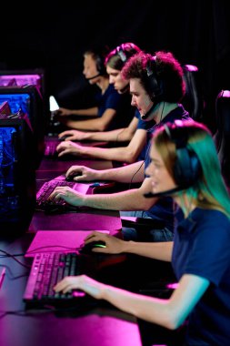 Siber yarışma sırasında bilgisayar monitörlerinin önünde uzun masa başında oturan kulaklıklı çağdaş video oyuncuları.