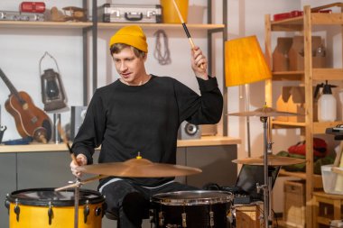 Siyah kotlu, kazaklı ve sarı bereli genç bir adam davul ve zillerin önünde otururken bagetleri yüksek tutuyordu.