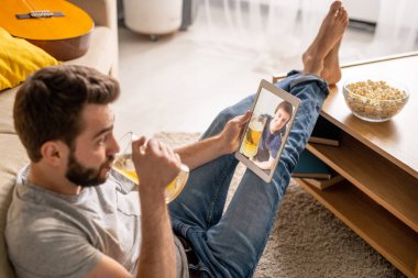 Karantina sırasında arkadaşınla konuşurken yerde oturup bira içen sakallı, rahat genç bir adam.