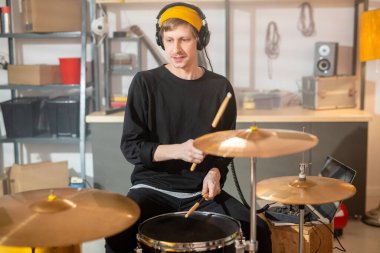 Kulaklıklı genç adam, sarı bereli, siyah kazaklı ve kot pantolonlu davul çalarken davul çalıyordu.