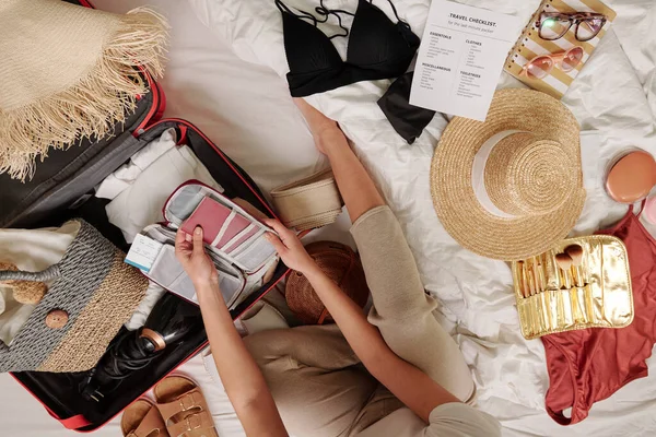 ビーチバケーションのための服や梱包スーツケースの間でベッドに座っている女性のビューの上 — ストック写真