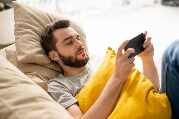 Allvarlig Ung Skäggig Man Med Gul Kudde Liggande Soffan Och — Stockfoto