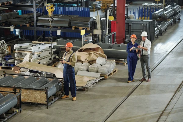 工場の倉庫で働く人々 彼の同僚は製品を議論しながら リモート制御と産業用クレーンを使用してひげそりの男 — ストック写真