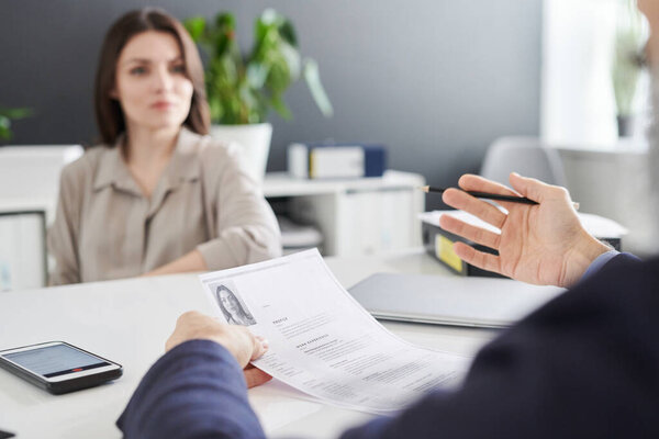 Hands of contemporary psychologist or employer with pen and resume of young female applicant explaining something during interview
