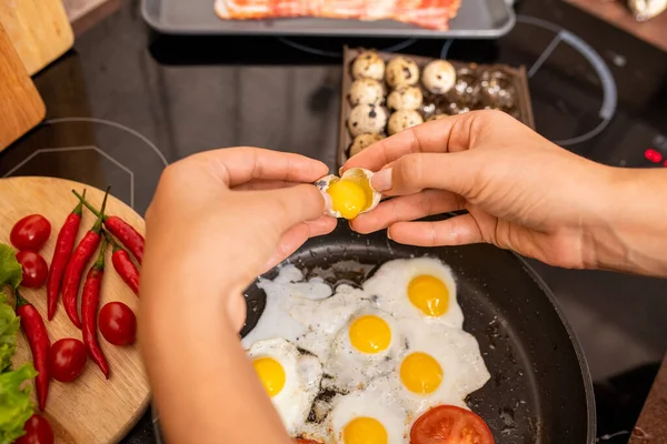 女性在厨房用蔬菜做早餐时 将新鲜鹌鹑蛋倒入热油锅的双手 — 图库照片