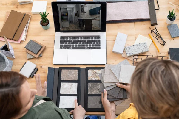 两名年轻的女性创意设计师坐在笔记本电脑前的桌子旁 讨论大理石瓷砖 油毡和家庭内部照片的样品 — 图库照片