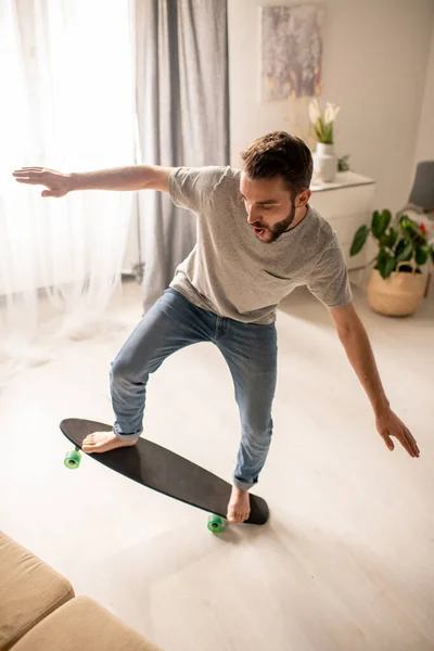 Jovem Barbudo Excitado Jeans Desfrutando Equilíbrio Skate Sala Estar Durante — Fotografia de Stock