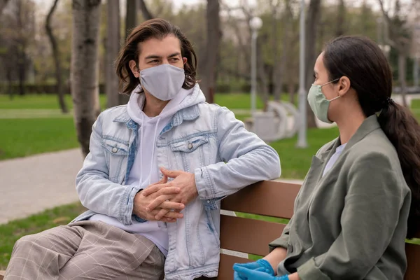 Pareja Joven Contemporánea Ropa Casual Máscaras Protectoras Sentadas Banco Madera —  Fotos de Stock