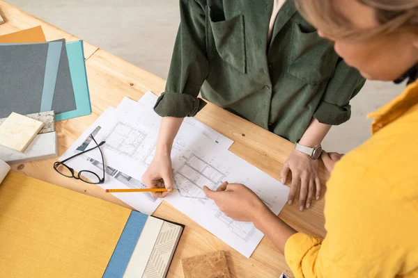 两名富有创造力的女设计师在工作会议上弯腰讨论带有新房子或公寓草图的文件时 坐在桌子上 — 图库照片