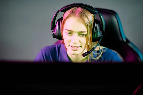 在俱乐部咨询客户或玩电子游戏的游戏玩家时 耳机里的年轻女性操作员看着电脑屏幕 — 图库照片