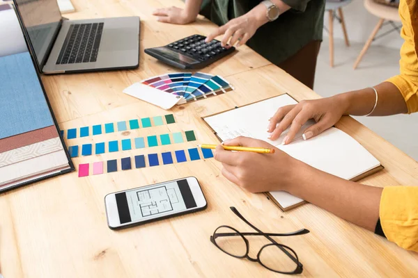 年轻的设计师用铅笔指着彩色的石板 同时在同事按下计算器按钮的背景下做笔记 — 图库照片
