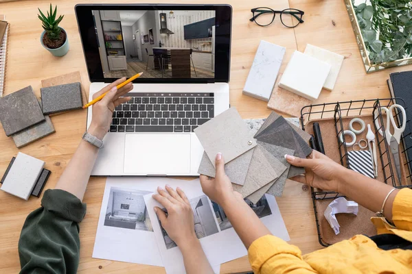 当代设计师在与手握油毡样品的同事协商时 在笔记本电脑显示屏上指向家中的内部示例 — 图库照片