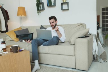 Röntgenli hasta sakallı bir adam dizlerinin üstünde kanepede oturuyor ve evde otururken internet doktoruna danışıyor.