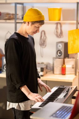 Sarı bereli genç müzisyenin yan görüntüsü ve siyah günlük giysi garajda yeni müzik kaydederken piyano tuşlarına dokunuyor.