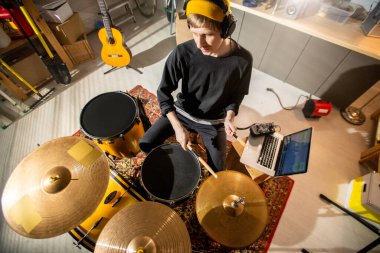Kulaklıklı genç müzisyen, davul ve zilleri çalarken dizüstü bilgisayarında yeni müzik kaydediyor.