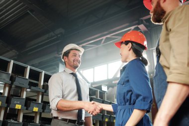 Çağdaş endüstriyel fabrika atölyesinde fabrika mühendisiyle sıkı sıkıya tokalaşan yakışıklı bir iş adamı.