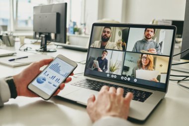 Boş ofiste çalışan işadamlarının yakın çekimleri ve video konferans uygulaması üzerinden iş arkadaşlarıyla satışları tartışırken grafiği görüntülemek için akıllı telefon kullanımı