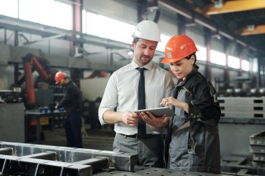 Tablet üzerinde mühendislik uygulaması kullanırlarken Asyalı metal uzmanı mühendisle teknik çizim hakkında konuşuyor.