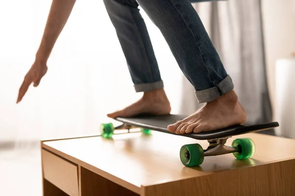 自宅でコーヒーテーブルの上に危険なスケートボードを練習ジーンズで認識できない男のクローズアップで隔離 — ストック写真