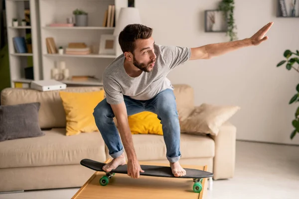 Joven Barbudo Extático Parado Monopatín Mientras Equilibra Mesa Café Mientras —  Fotos de Stock