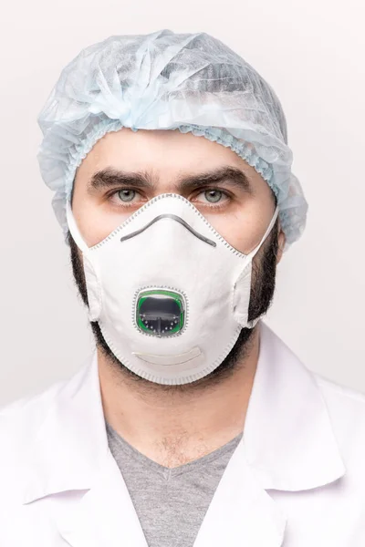 医療用キャップ ホワイトコート 保護眼鏡 隔離されたカメラの前に立つ呼吸器の若い深刻な外科医や医師 — ストック写真