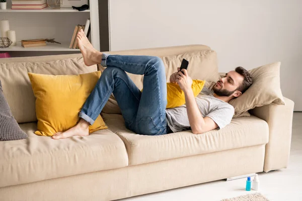 Jeune Homme Barbu Sérieux Jeans Couché Sur Canapé Communiquant Ligne — Photo