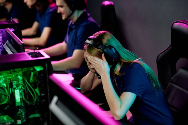 在视频游戏玩家的背景下 头戴耳机 弯腰坐在电脑显示器前 摸着头的疲惫或失败的女孩 — 图库照片