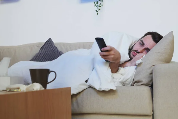 Joven Enfermo Con Control Remoto Acostado Sofá Debajo Manta Con — Foto de Stock