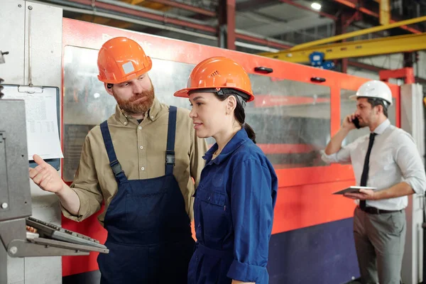 硬帽教学中的轴承操作员教亚洲学员在现代工厂车间使用数控机床 — 图库照片