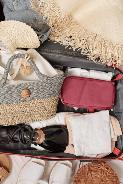 Above view of womens stuff such as cosmetic case. Summer bag, clothes, hairdryer in suitcase