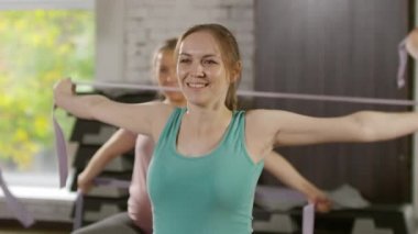 Spor salonunda omuz dairesi çizerken bandı kullanan neşeli ve motive olmuş hamile bir kadının orta boy fotoğrafı.