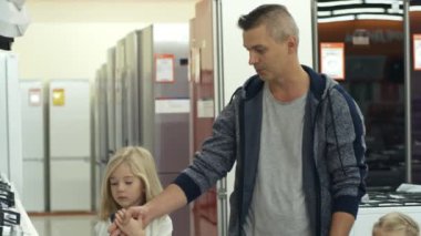 Babam iki küçük tatlı kızla el ele tutuşurken ev gereçleri mağazasında dolaşıp mutfak sobasını seçiyor.