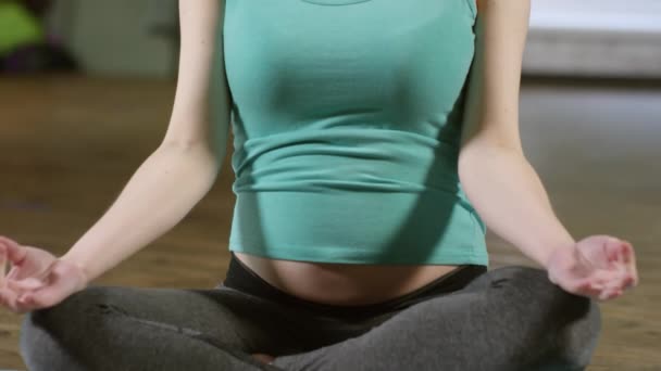 Naklonit se střední záběr mladé těhotné ženy ve sportovním oblečení sedí v lotosu pózovat na podložce jógy a cvičení meditace