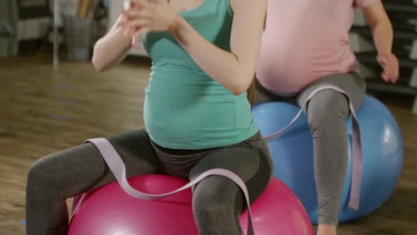 安定したボールの上に座っている2人の妊婦のショットを傾け フィットネスクラスの前にストレッチ練習でウォーミングアップ — ストック動画