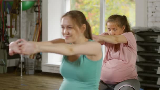 安定したボールの上に座って フィットネスクラス中に腕のためのストレッチ練習を行う2人の妊婦 — ストック動画